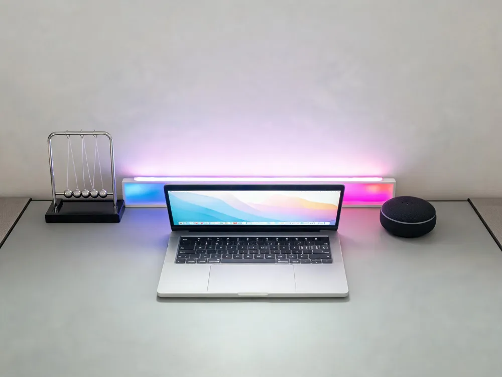 A colorful LED light bar behind a laptop, a quirky desk toy, and a smart speaker, adding personality to a home office.
