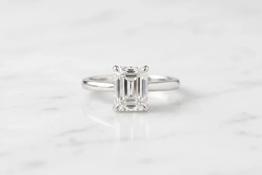 The classic solitaire serves as the perfect minimalist framework to showcase the architectural brilliance and hall-of-mirrors effect of an emerald-cut stone.