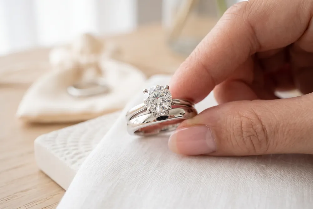 Tradition places the wedding band closest to the heart, with the engagement ring stacked above, creating a meaningful and graceful arrangement.