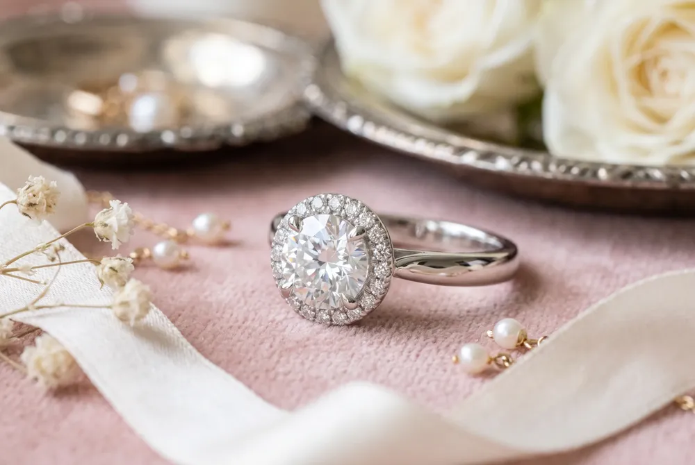 A white sapphire center stone surrounded by a halo of smaller gems creates the illusion of a much larger, more opulent ring, echoing vintage Hollywood glamour at a fraction of the cost.
