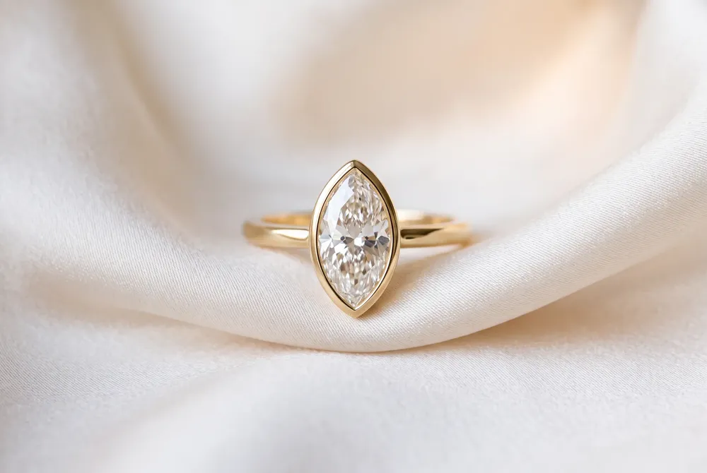 A refined bezel frames the marquise in a sleek rim of metal, offering coverage around its pointed ends.