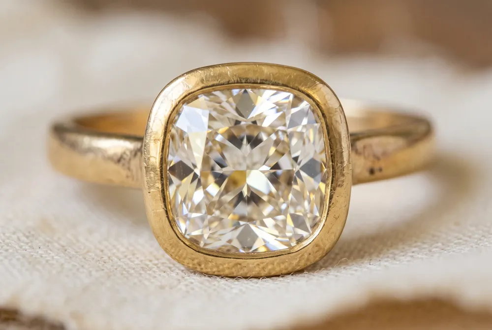 A bezel setting wraps the diamond in a sleek metal frame, offering enduring protection and a distinctly vintage character that enhances the warm, heirloom appeal of a cushion cut diamond.