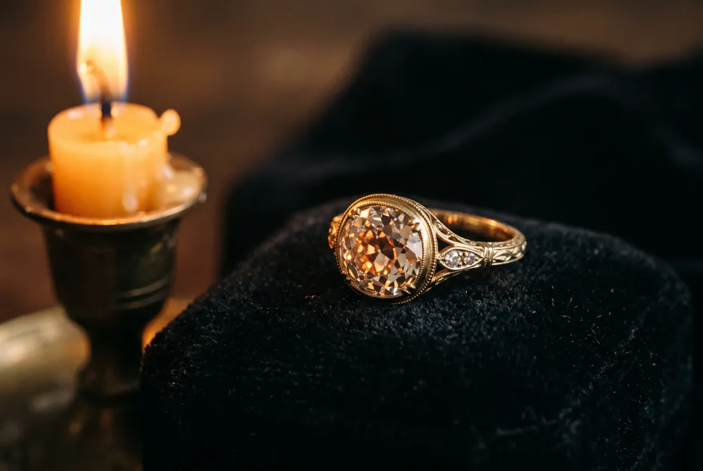 The ring's antique old mine brilliant cut diamond and hand-engraved 18K yellow gold setting evoke heirloom artistry and romantic candlelit sparkle.