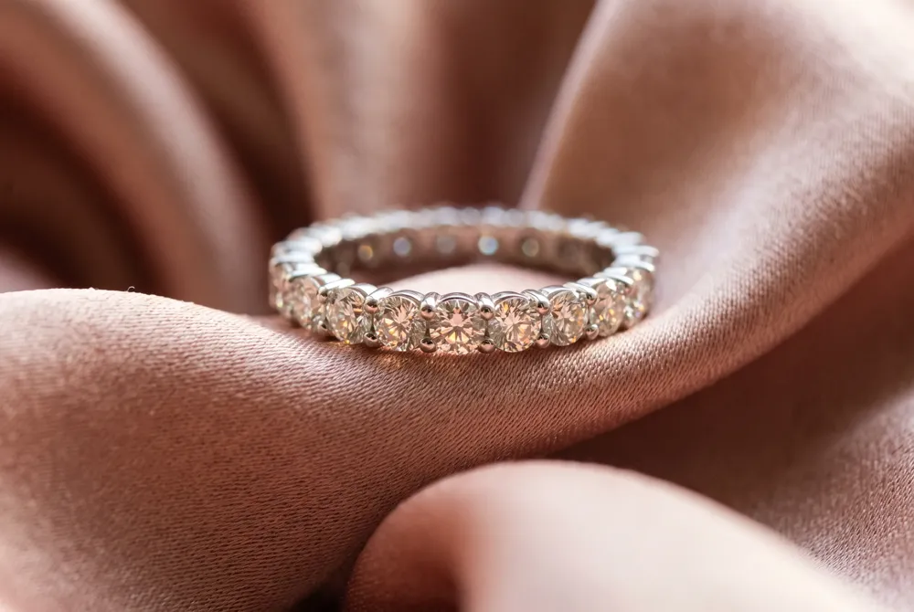 A round full eternity band offers uninterrupted brilliance, with round moissanite stones set around the entire band for timeless sparkle that complements a solitaire or halo engagement ring.