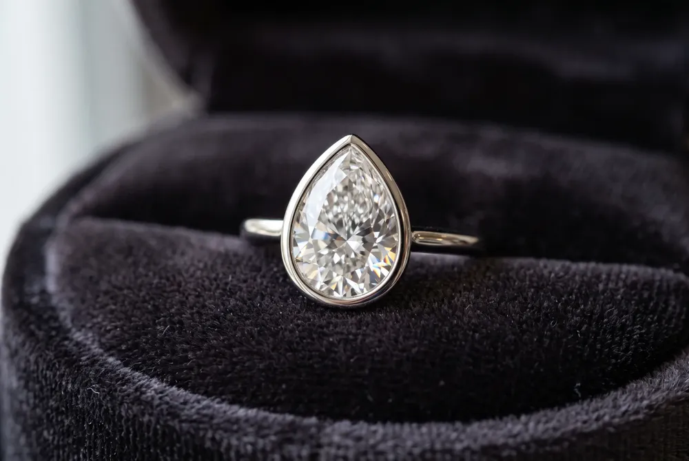 A bezel setting cradles the pear-shaped diamond in a sleek metal rim, offering timeless elegance and lasting protection.
