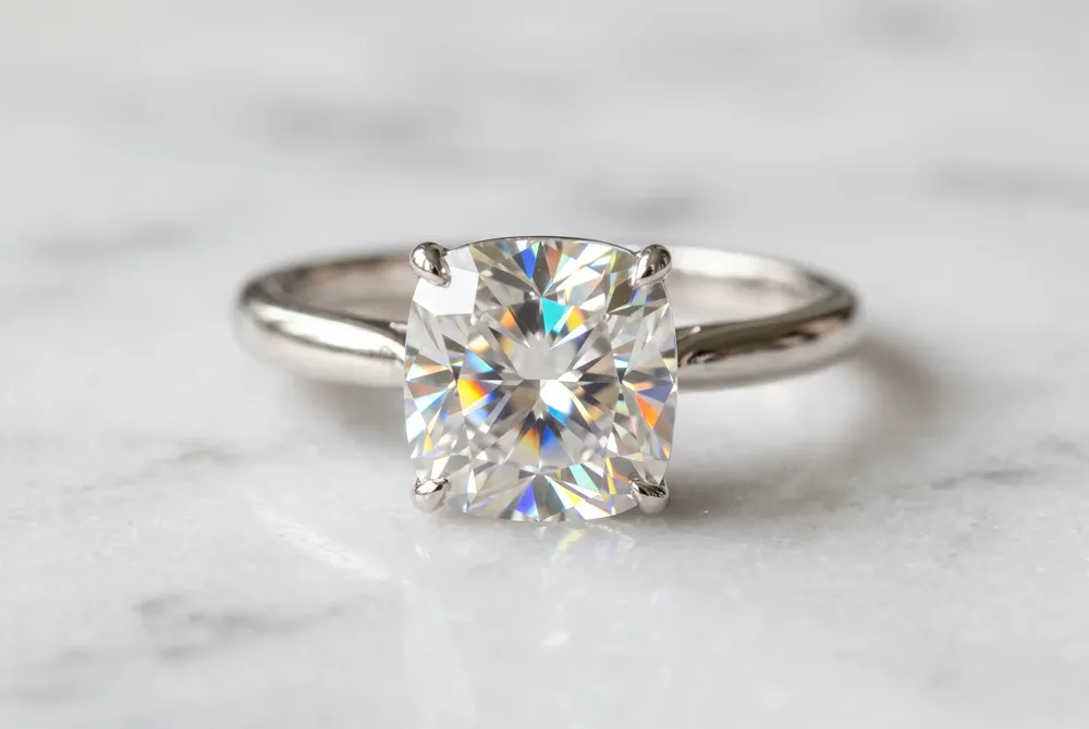 The cushion cut offers a softer, warmer sparkle than the round brilliant, with broad facets that magnify the moissanite's mesmerizing rainbow flashes.
